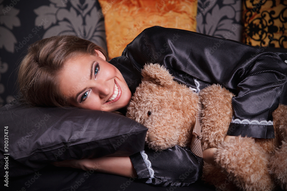 Beautiful young woman hugging a teddy bear in the bed