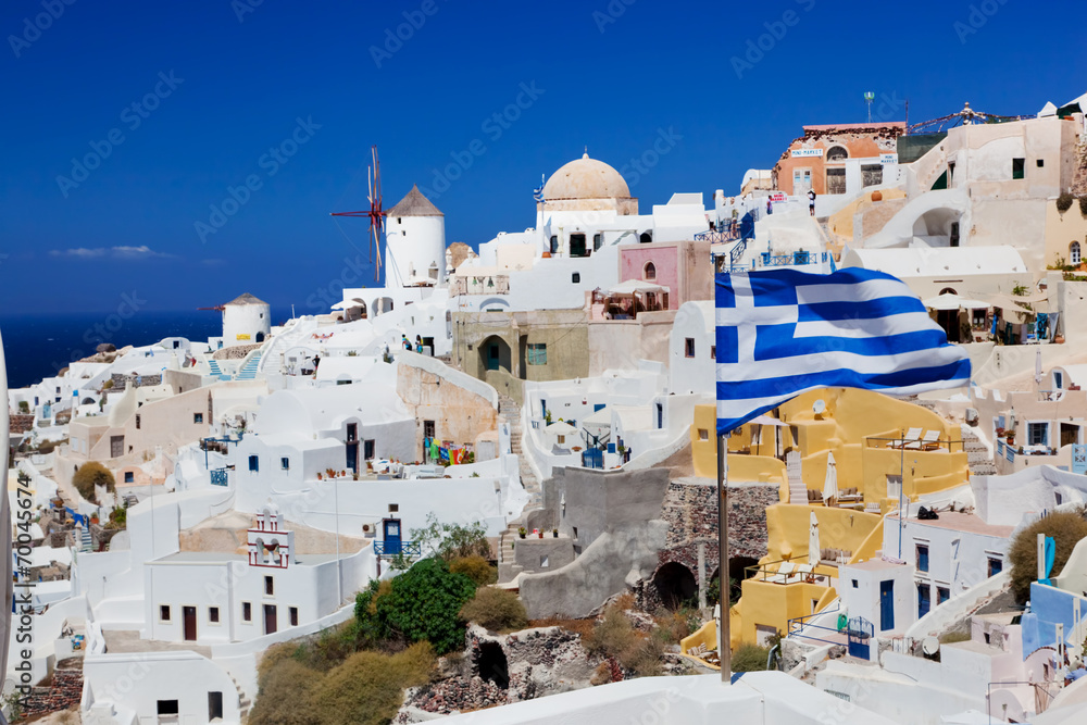 Oia town on Santorini island, Greece. Waving Greek flag
