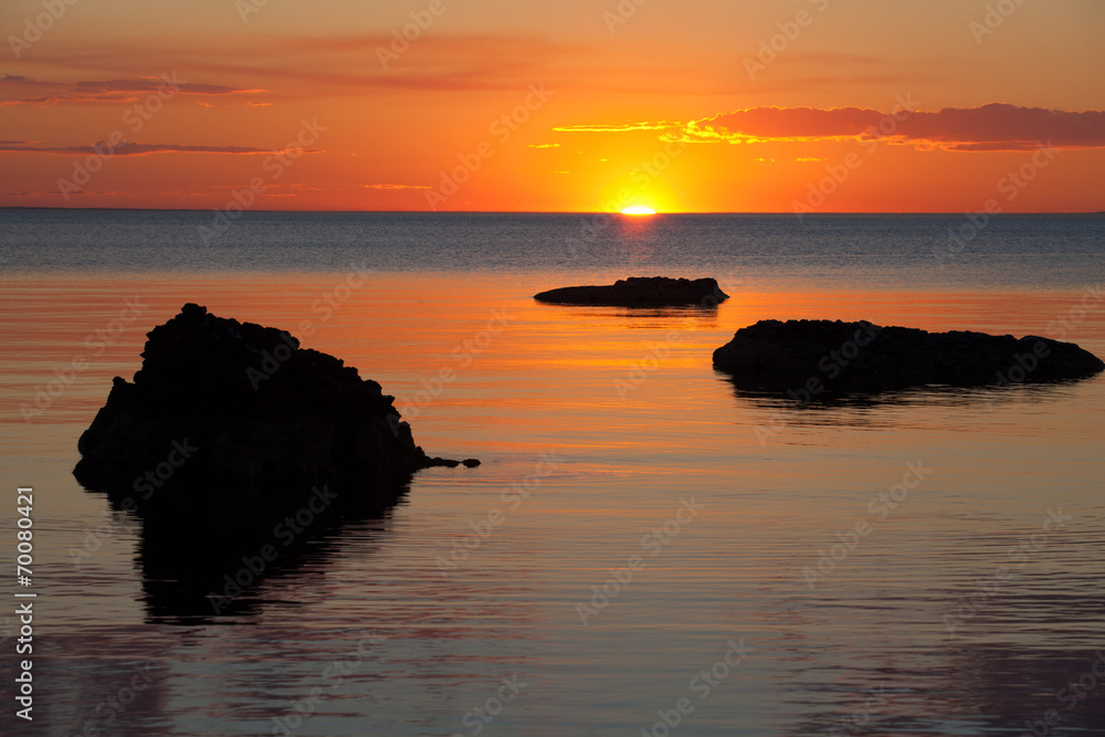 Vivid orange sunset over water, with rock silhouettes