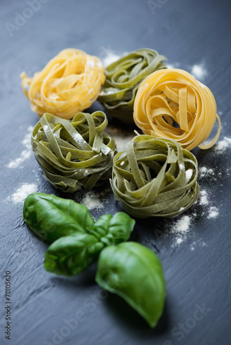Raw colored tagliatelle with green basil leaves, studio shot