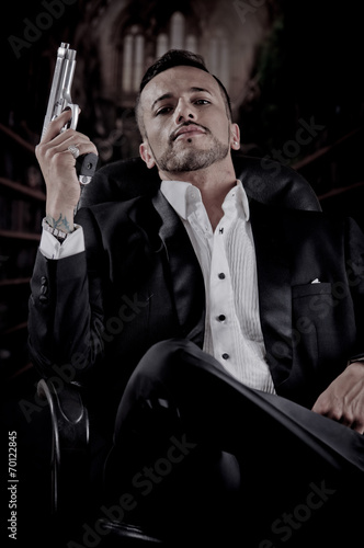 Elegant man sitting in a chair holding gun over dark background