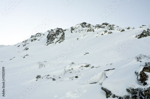 black rocks covered by a layer of white snow, clear sky cooltone