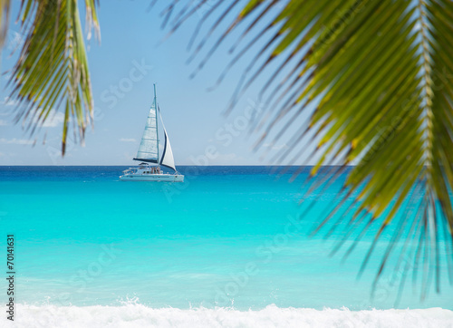 Tropical beach with yacht and palm leaves. Praslin, Seychelles