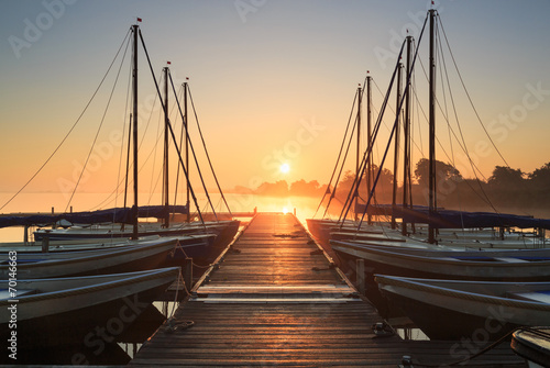 Tranquil, foggy sunrise at a pier with sailing boats.