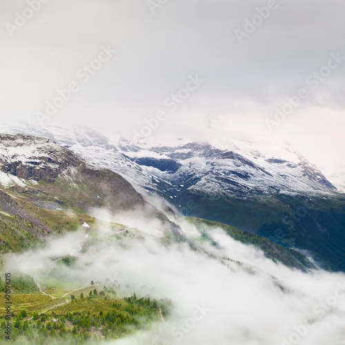 Snowy and misty peaks of Alps mountains above valley.