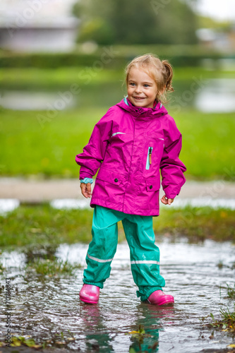 Happy little girl plays in a puddle