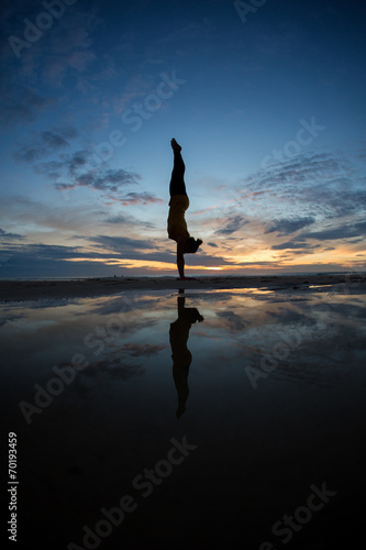 Fototapet girl doing handstand on beach in sunset