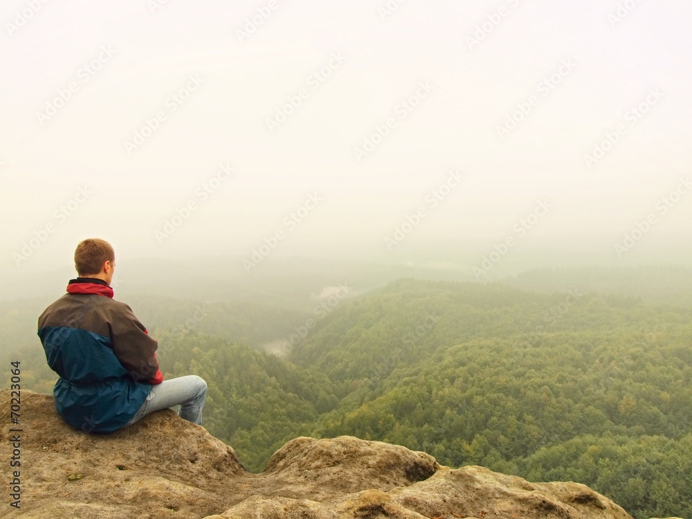 Sad man sit  on the peak of sandstone rock and watching down