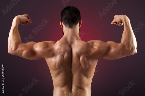 Young bodybuilder showing his back muscles on a dark background