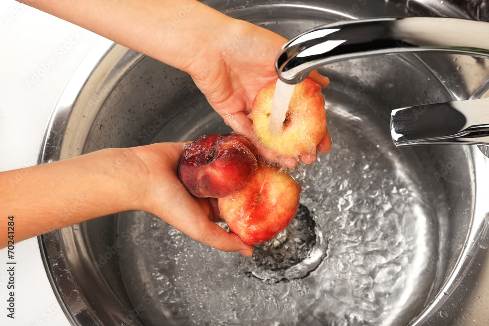 Woman's hands washing peaches in sink