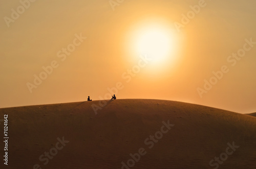 Silhouettes of sitting and talking friends on a sand hilll