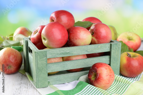 Sweet apples in wooden box on table on bright background