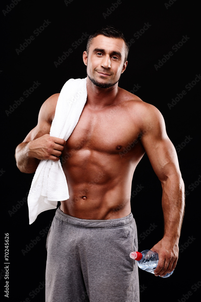 Fototapeta premium Handsome muscular sportsman holding towel and bottle with water