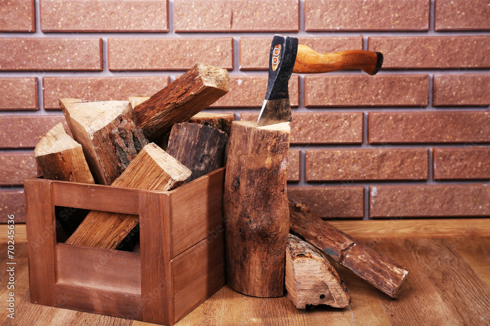 Box of firewood and axe on floor on brick background