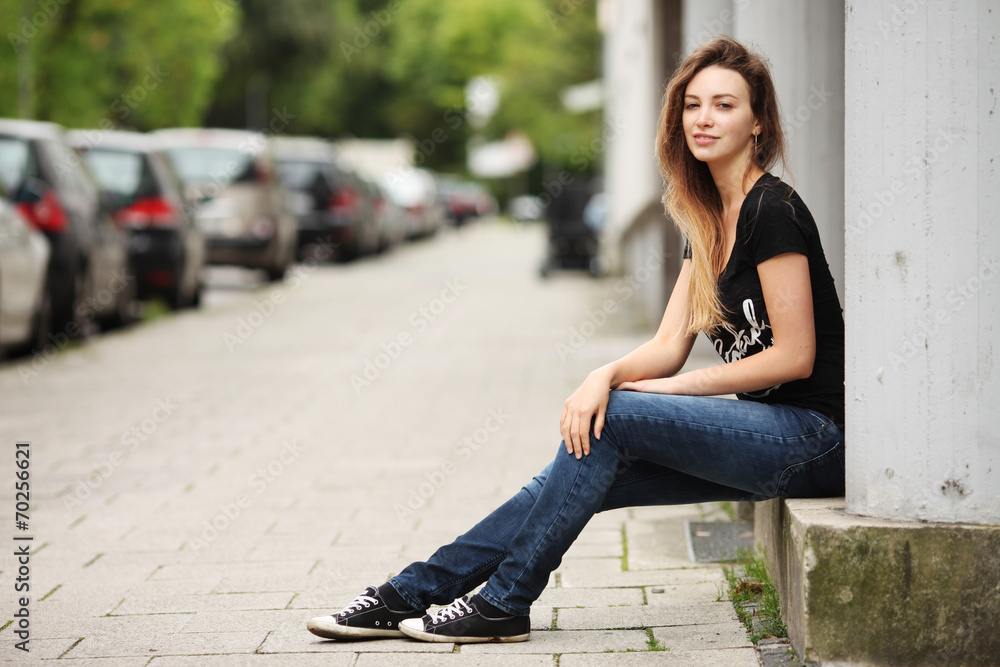 Fototapeta premium Junge Frau sitzt auf Mauer