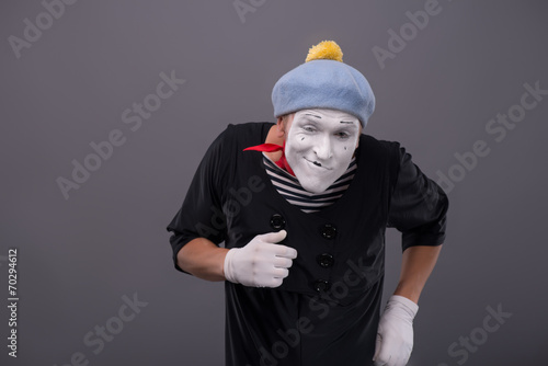 Portrait of young male mime with white face, grey hat showing em