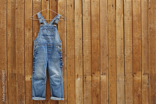 Pair of denim dungarees hanging against wooden wall. photo