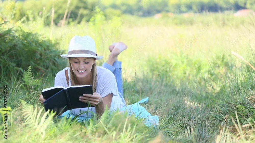 Smiling woman laying in grass and reading book Smiling woman laying in grass and reading book