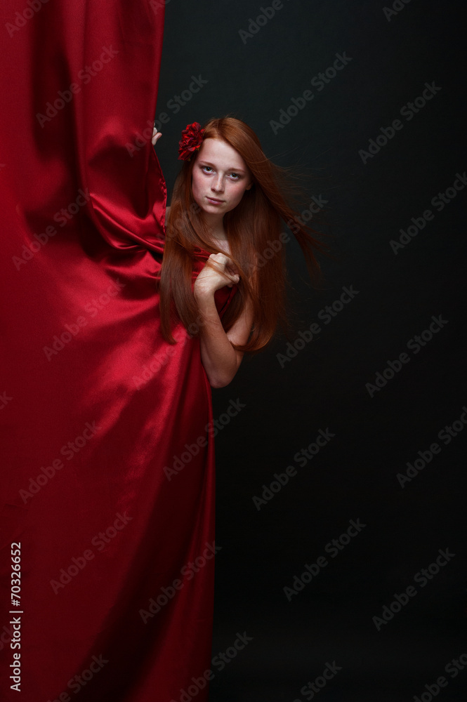 Beautiful red-haired girl looks out from behind a red theater cu