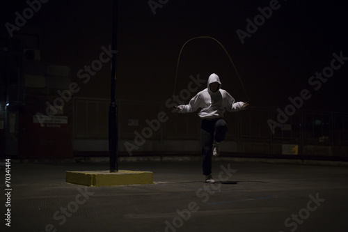 Hooded athlete skipping under a street light at night