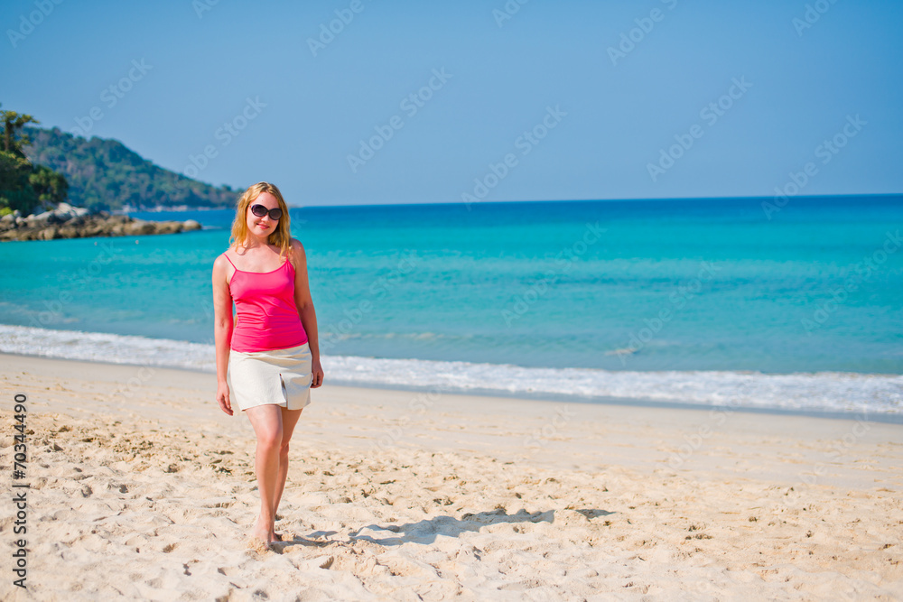 Young woman in pink top and beige skirt walking on beach