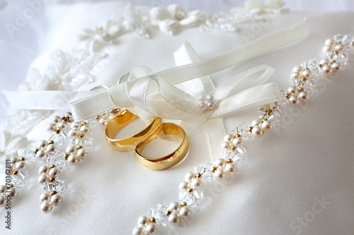 Gold wedding rings on a pillow with ribbons