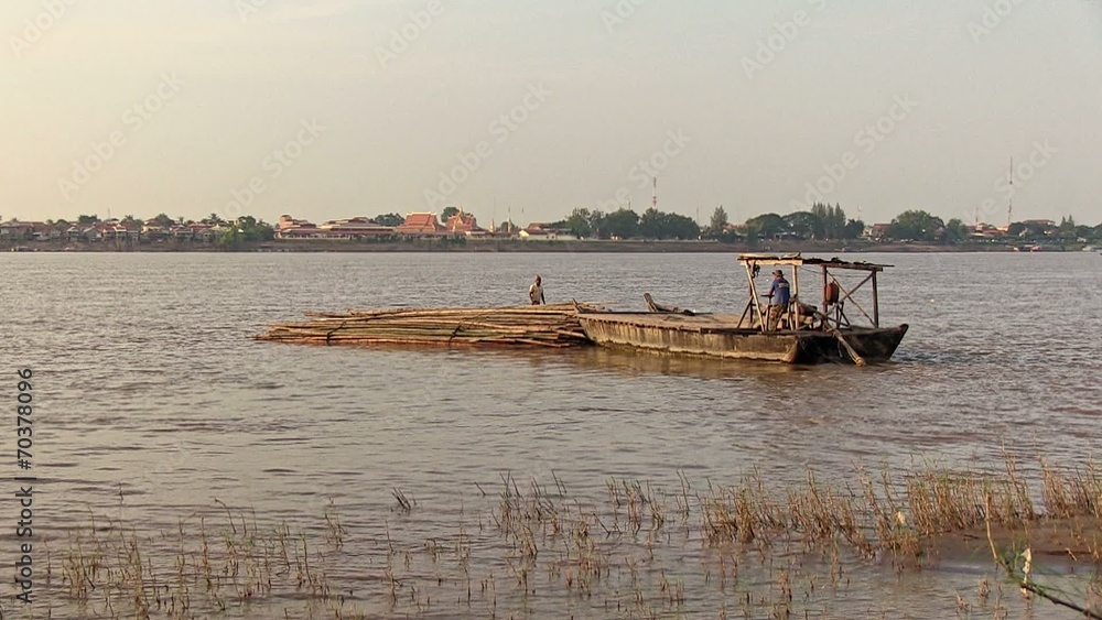 Small barge towing from the bow a heap of bamboo poles and drawing away from the riverside Small barge towing from the bow a heap of bamboo poles and drawing away from the riverside