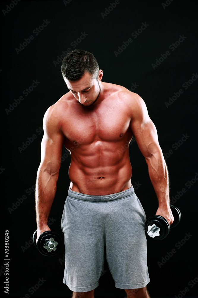 Portrait of muscular man holding dumbbells on black background