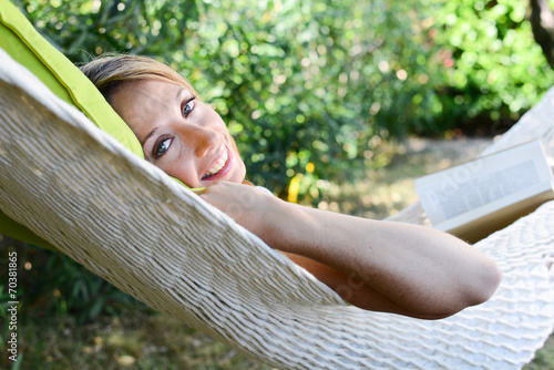 cheerful young woman reading a book in a hammock