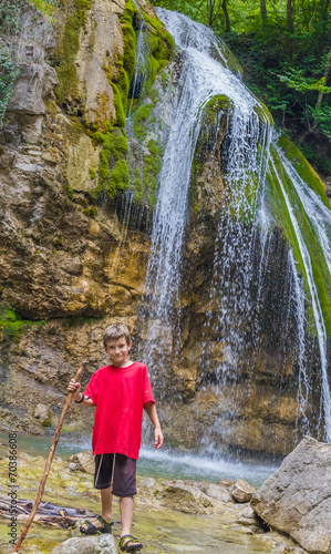 young happy smiling child boy on waterfall background