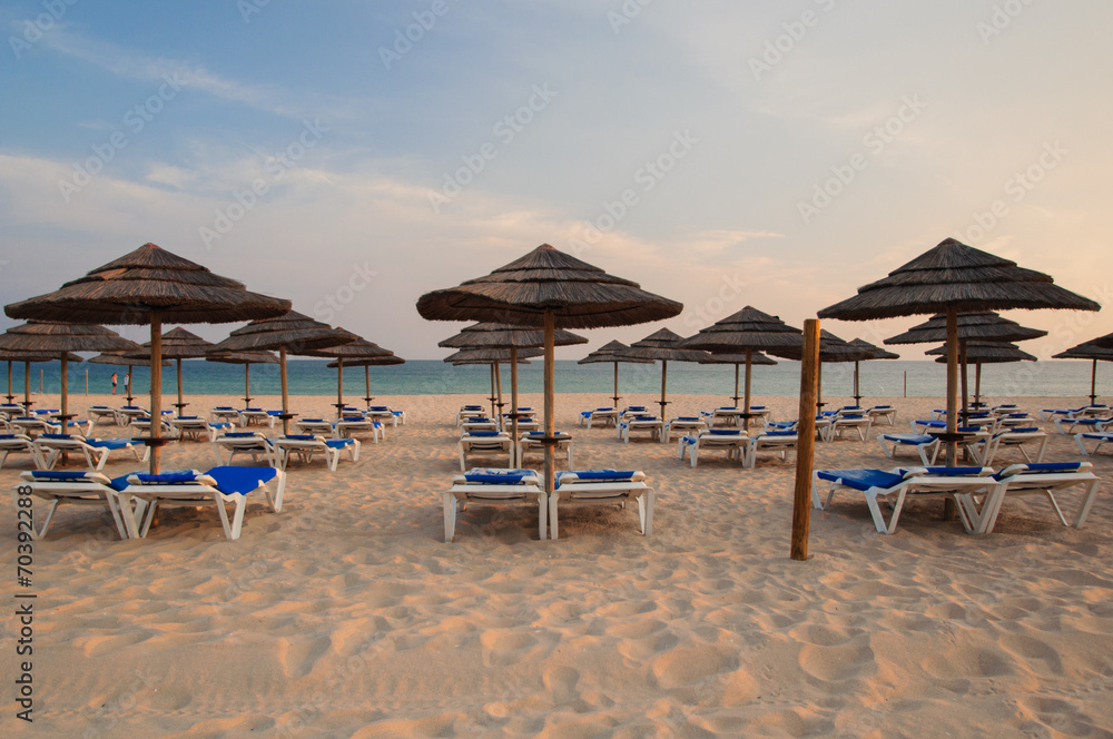 Umbrellas and deck lounges in the beach at sunset. Algarve