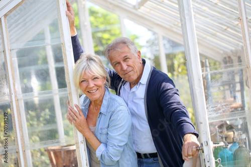 Senior couple standing by greenhouse in garden