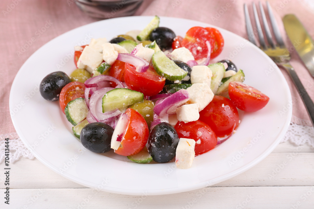 Greek salad served in plate on napkin on wooden background