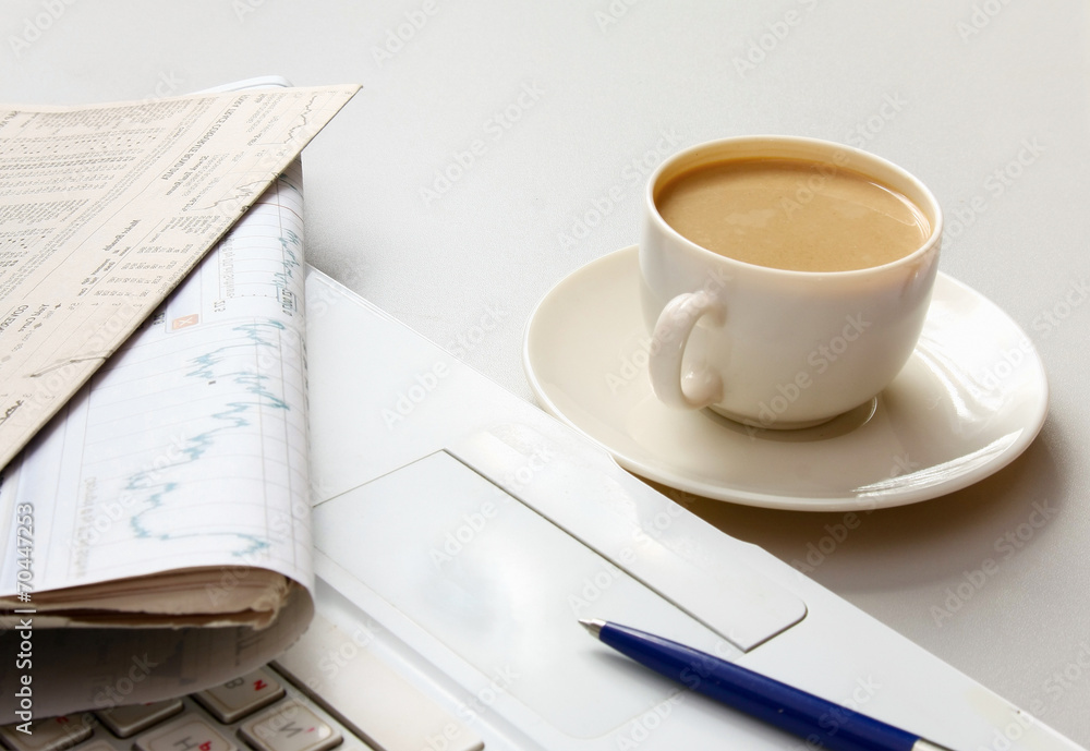 Cup of coffee near the laptop and newspapers Cup of coffee near the laptop and newspapers