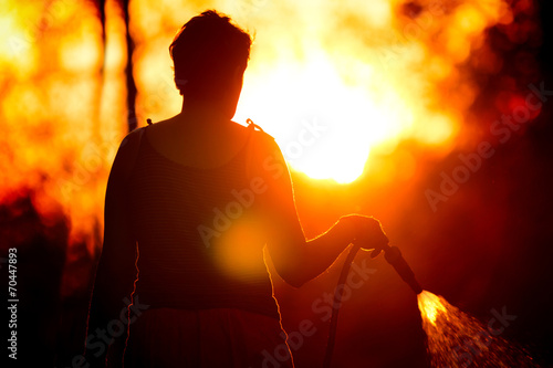 Silhouette of a woman watering grass at sunset
