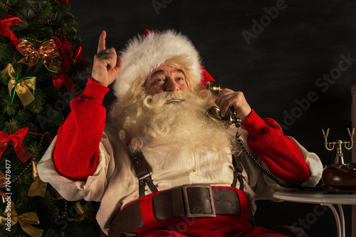 Portrait of emotional Santa Claus calling phone at home