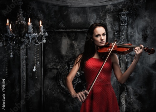 Young woman in red dress playing violin in mystic interior