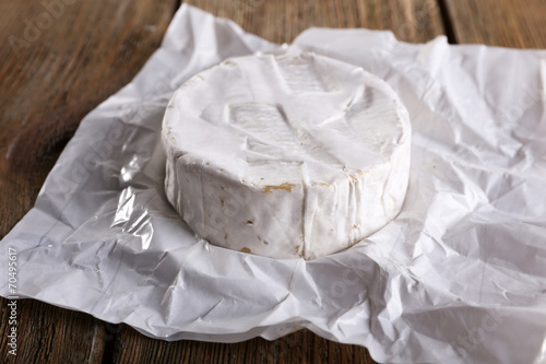 Camembert cheese on paper on wooden background