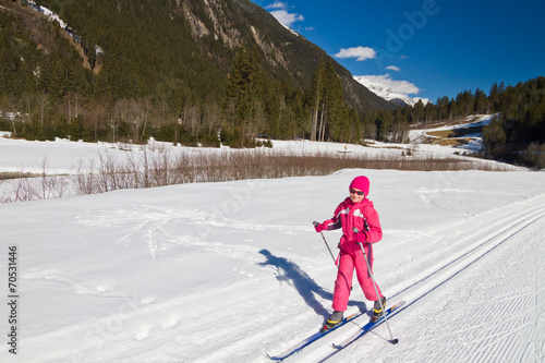 Cute little girl enjoying cross country skiing on a beautiful sunny day. Valley in Austrian Alps
