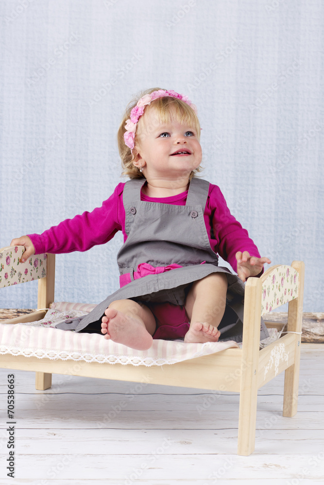 Happy little baby girl sitting on the small bed Happy little baby girl sitting on the small bed