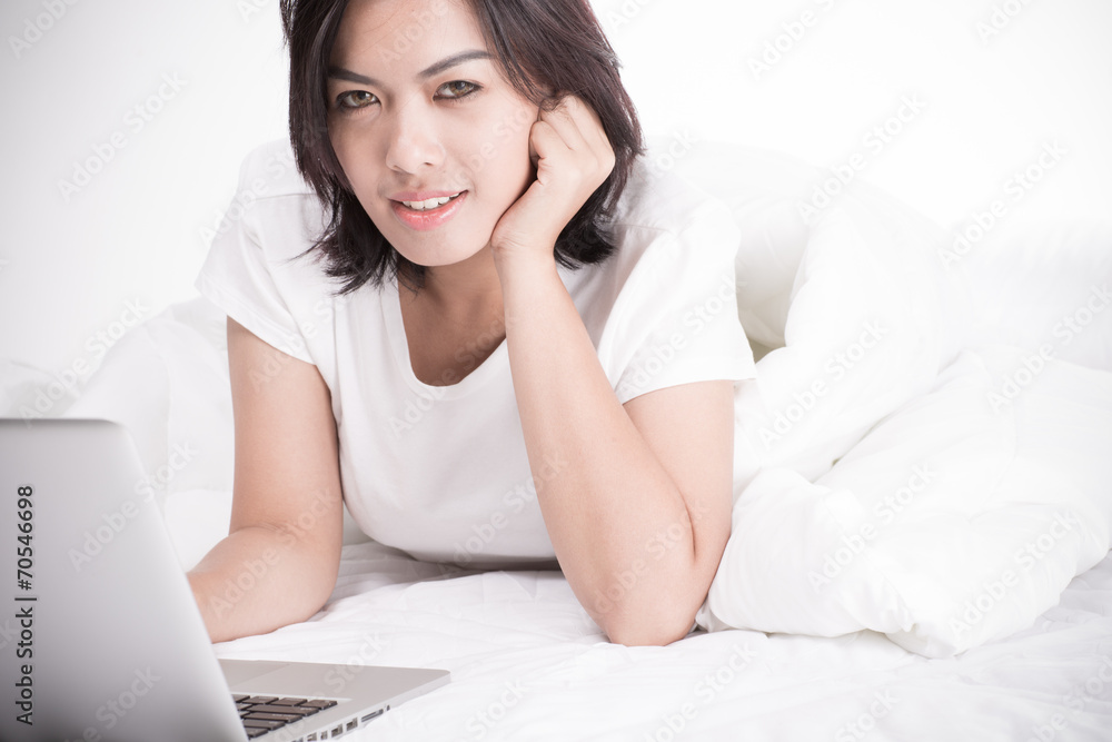 Smiling woman using a laptop while lying on her bed Smiling woman using a laptop while lying on her bed