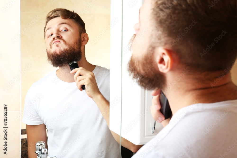 Obraz premium Young man shaving his beard in bathroom