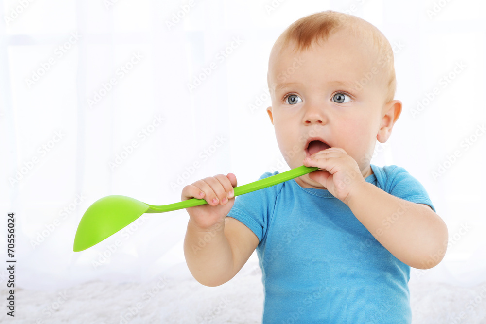Cute baby boy with kitchen spoon on carpet in room Cute baby boy with kitchen spoon on carpet in room