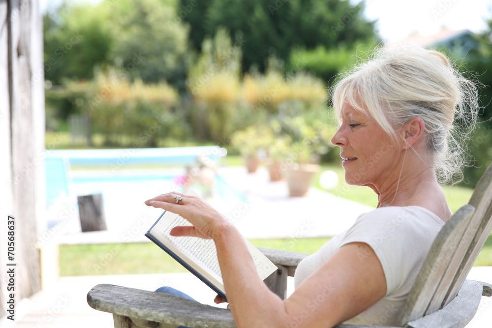Senior woman reading book by swimming-pool Senior woman reading book by swimming-pool