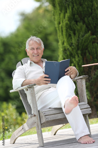 Senior man reading book in pool deck chair