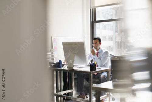 A man seated at a desk in an office, using a computer. photo