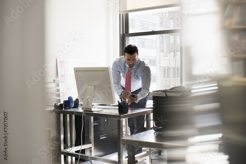 A man standing at his desk using his phone, dialling or texting. photo