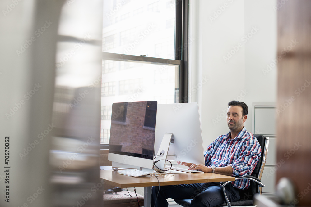 A man working in an office at a desk using a computer. A man working in an office at a desk using a computer.