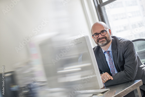 Office life. A man in a suit and tie sitting at his desk looking around his computer. photo