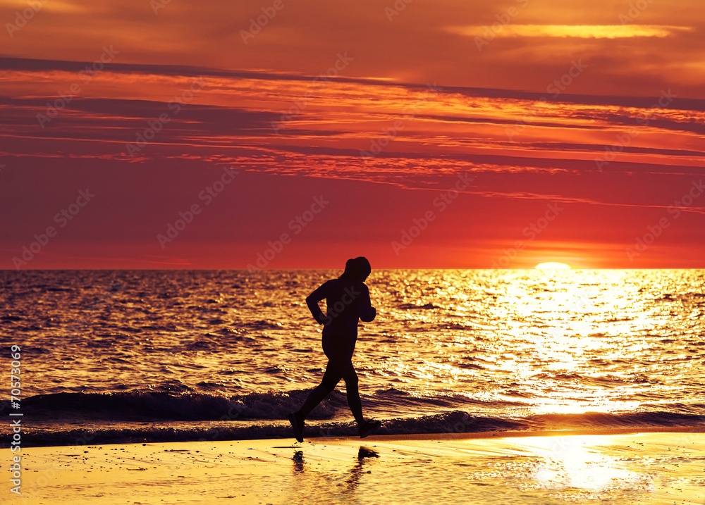 Female jogger running on beach at sunset.